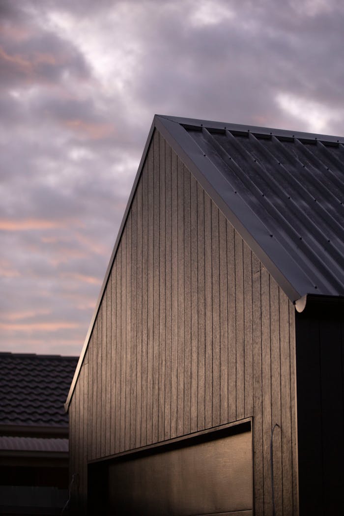 Home A modern house with a sleek metal roof stands against a dramatic cloudy sky.